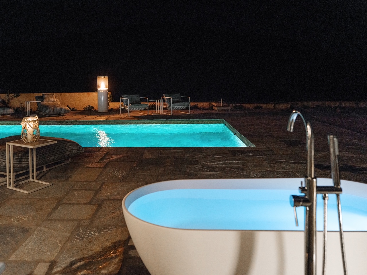 Romantic night view of outdoor bathtub beside glowing pool at Patmos adults-only retreat