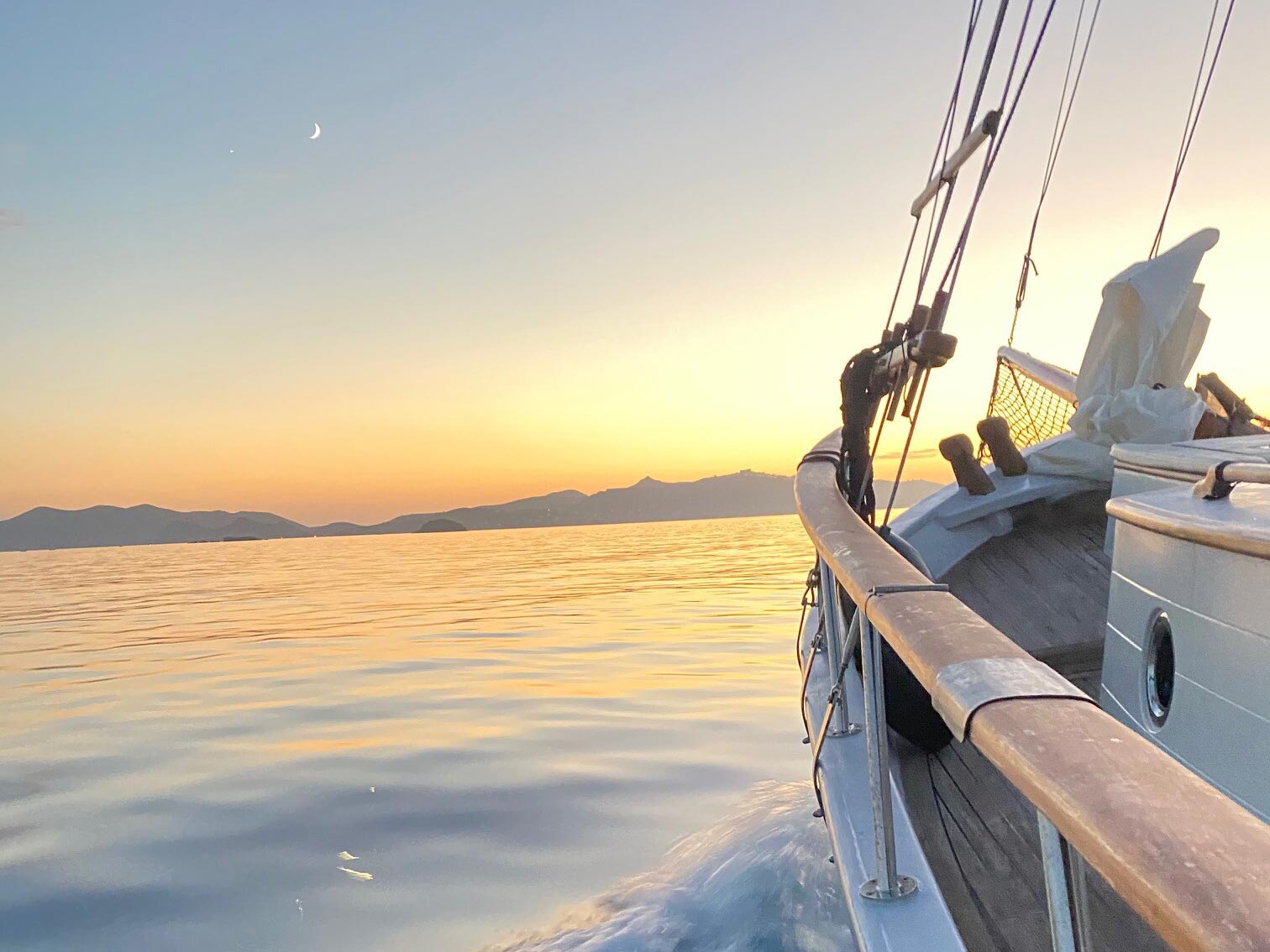 Sailing boat at sunset near Patmos island with calm Aegean waters and mountain views